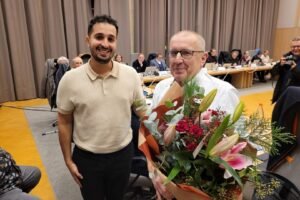 Gemeenteraadsvoorzitter Achraf El Yakhloufi schenkt Luc Debondt een bos bloemen bij zijn laatste gemeenteraad_